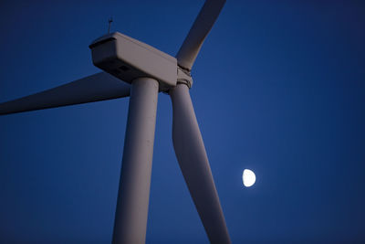 Looking up at wind turbine against a dusk blue sky with the moon