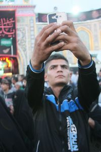 Midsection of man holding mobile phone in city at night