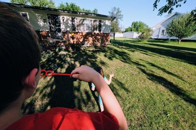 Rear view of boy blowing bubbles while playing with sister at yard