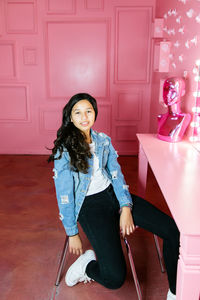 Young girl wearing a denim jacket sitting in a pink room