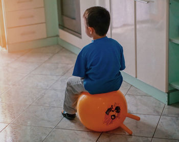 Rear view of boy sitting on balloon at home