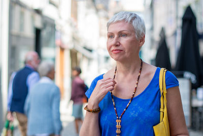 Stylishly dressed middle-aged woman with short gray hair, wearing blue shirt and holding yellow bag