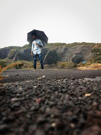 Woman standing on wet road against sky during rainy season