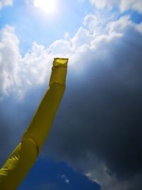 Low angle view of hand holding yellow umbrella against sky