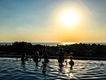 People swimming in pool against sky during sunset