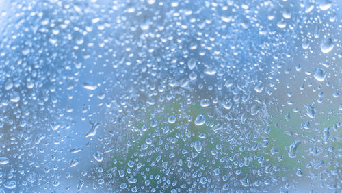 Full frame shot of wet glass window rainy weather, close up water droplets on blue windowshield 