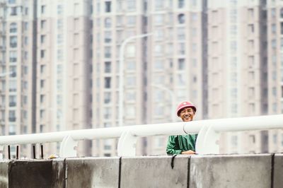 Portrait of happy man standing on bridge against buildings