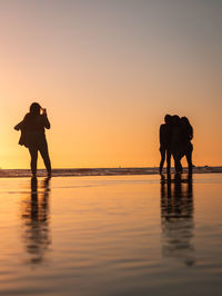 Silhouette people standing on beach against sky during sunset