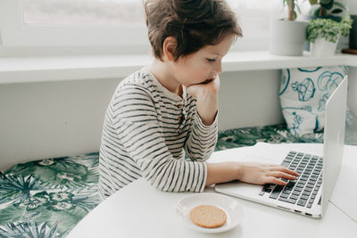 Little boy siting at the kitchen and look at the laptop. high quality photo