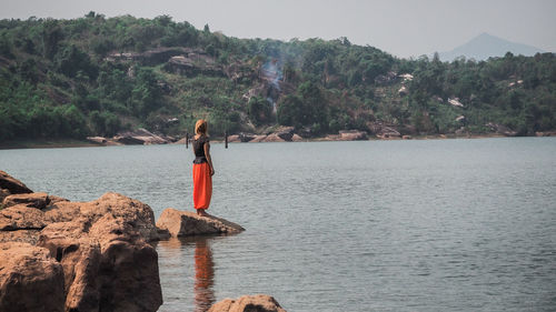 Woman on rock by sea against sky