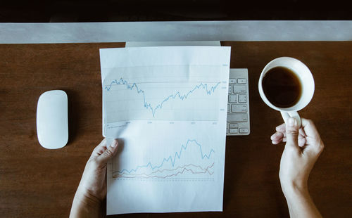 Cropped hand holding graph paper by coffee on desk