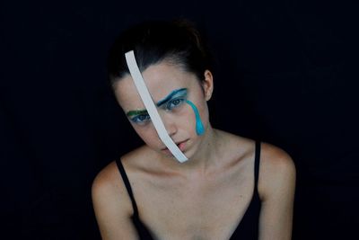 High angle portrait of young woman with paper and face paint against black background