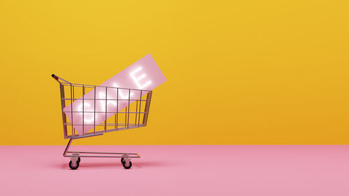 Close-up of shopping cart against yellow background