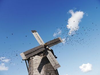 Low angle view of birds and windmill against sky