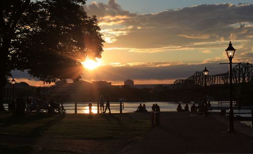 Silhouette people by river against sky during sunset