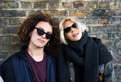 Portrait of couple in sunglasses against brick wall