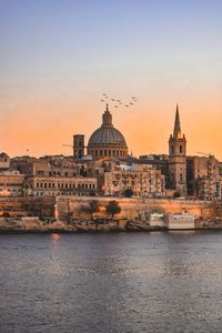 Buildings by river during sunset