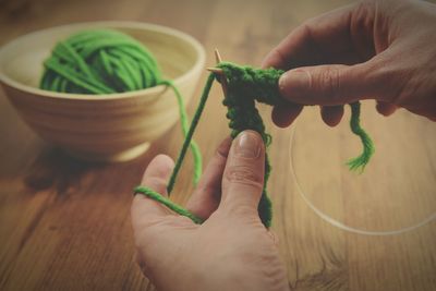 Cropped hands knitting green wool on table at home