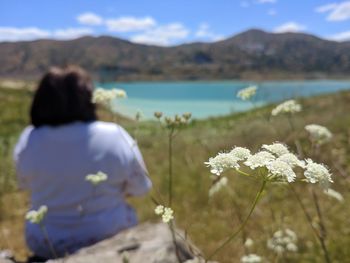 Rear view of person by flowering plants against sky