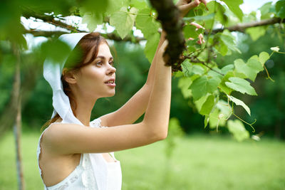 Side view of young woman standing against plants