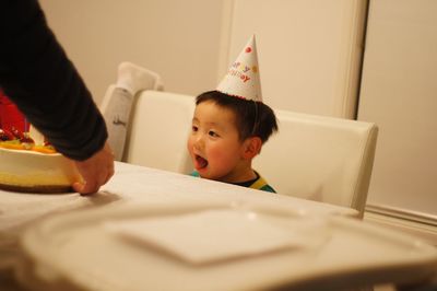 Thoughtful boy wearing party hat while sitting at table during birthday