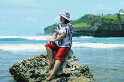 Side view of woman sitting on rock at beach
