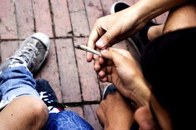 Low section of male friends smoking marijuana joint while sitting outdoors