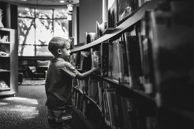 Side view of boy standing by bookshelf in library