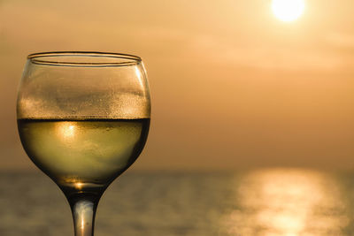 Close-up of champagne flute against sea at sunset