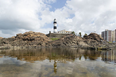 Lighthouse by buildings against sky