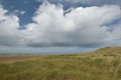 Scenic view of beach with dunes and cloudy sky