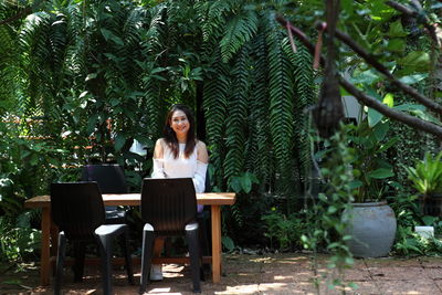 Young woman sitting on chair against plants