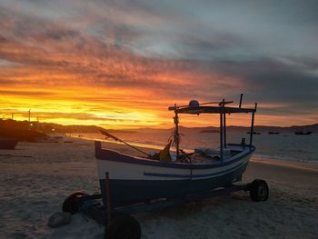 Boat moored on beach against sky during sunset