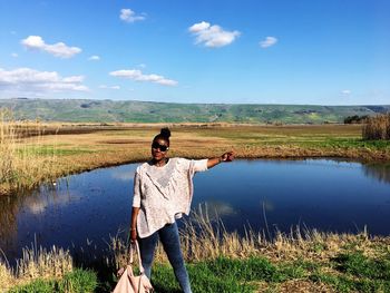 Woman standing at lakeshore against sky at golan heights on sunny day