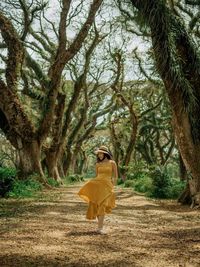 Woman wearing dress walking on land against trees in forest