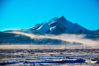 Scenic view of snow covered mountains against clear blue sky