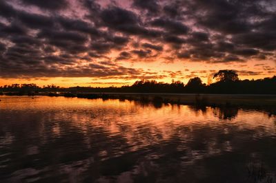 Scenic view of lake against cloudy sky at sunset