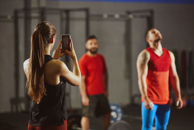 Woman photographing through mobile phone while standing at gym