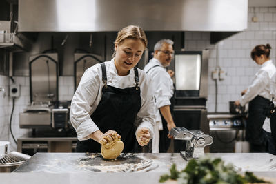 Young female chef kneading dough on kitchen counter in restaurant
