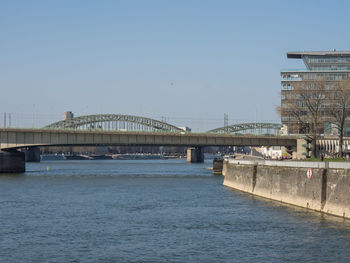 Bridge over river by buildings against clear sky