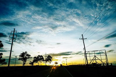 Silhouette road by electricity pylon against sky during sunset