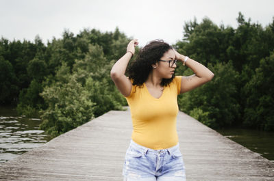 Woman with hand in hair looking away while standing against trees