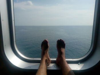 Low section of man by airplane window against sea