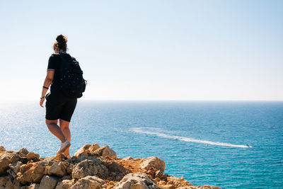 Rear view full length of woman on rocks against sea