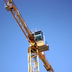 Low angle view of crane against clear blue sky