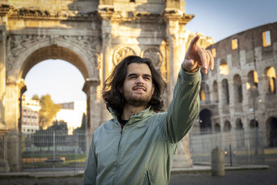 Young smiling man poses for a photo in front of the arch of titus.he is pointing the right direction
