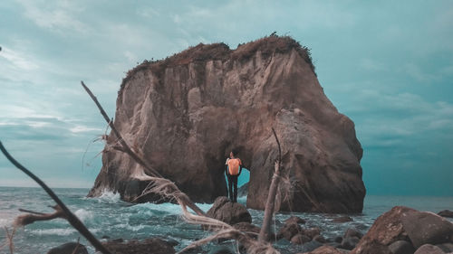 Man standing on rock by sea against sky