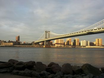 Suspension bridge over river against cloudy sky