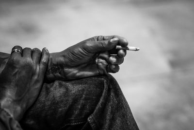 Close-up of man holding cigarette against sky