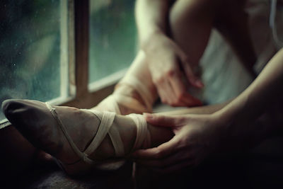 Low section of woman wearing ballet shoe while sitting on window sill